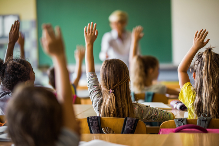 Back view of elementary students raising their arms on a class