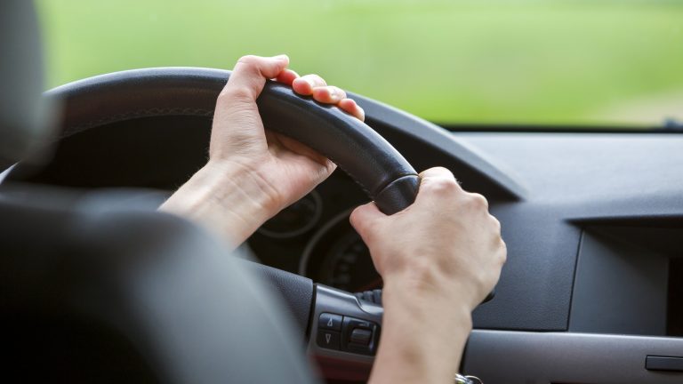 Woman hands on steering wheel driving a car